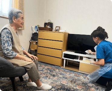 部屋の中を介護職員が掃除している様子を利用者が椅子に座って見ている写真